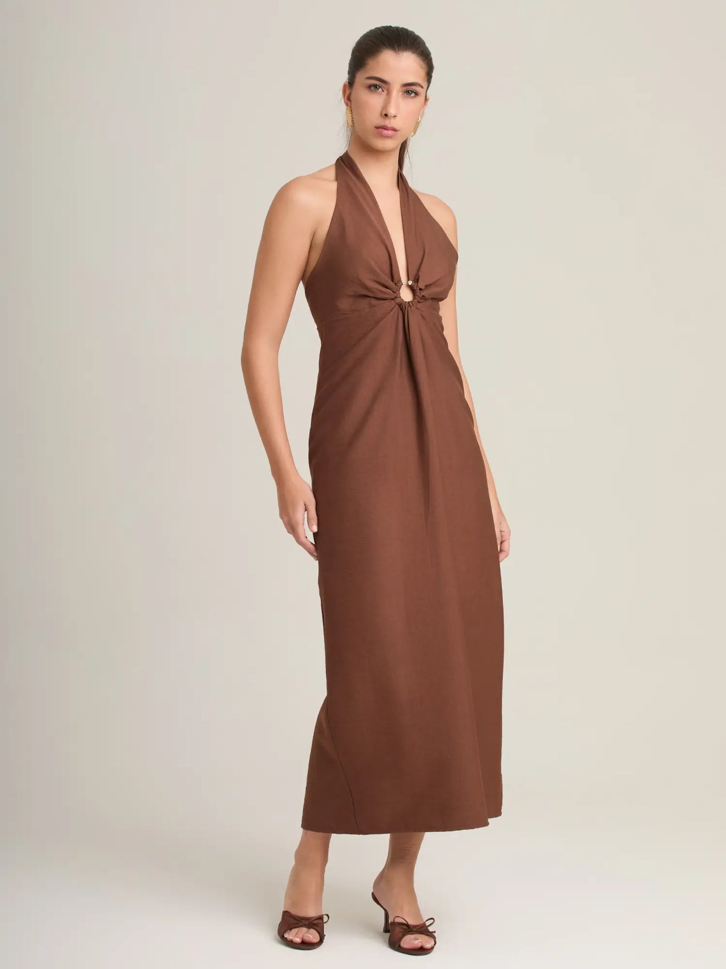 Este vestido marrón elegante ofrece un escote halter con un pequeño cut-out decorado por una argolla que añade personalidad. Su silueta limpia lo hace ideal para looks chic y atemporales.