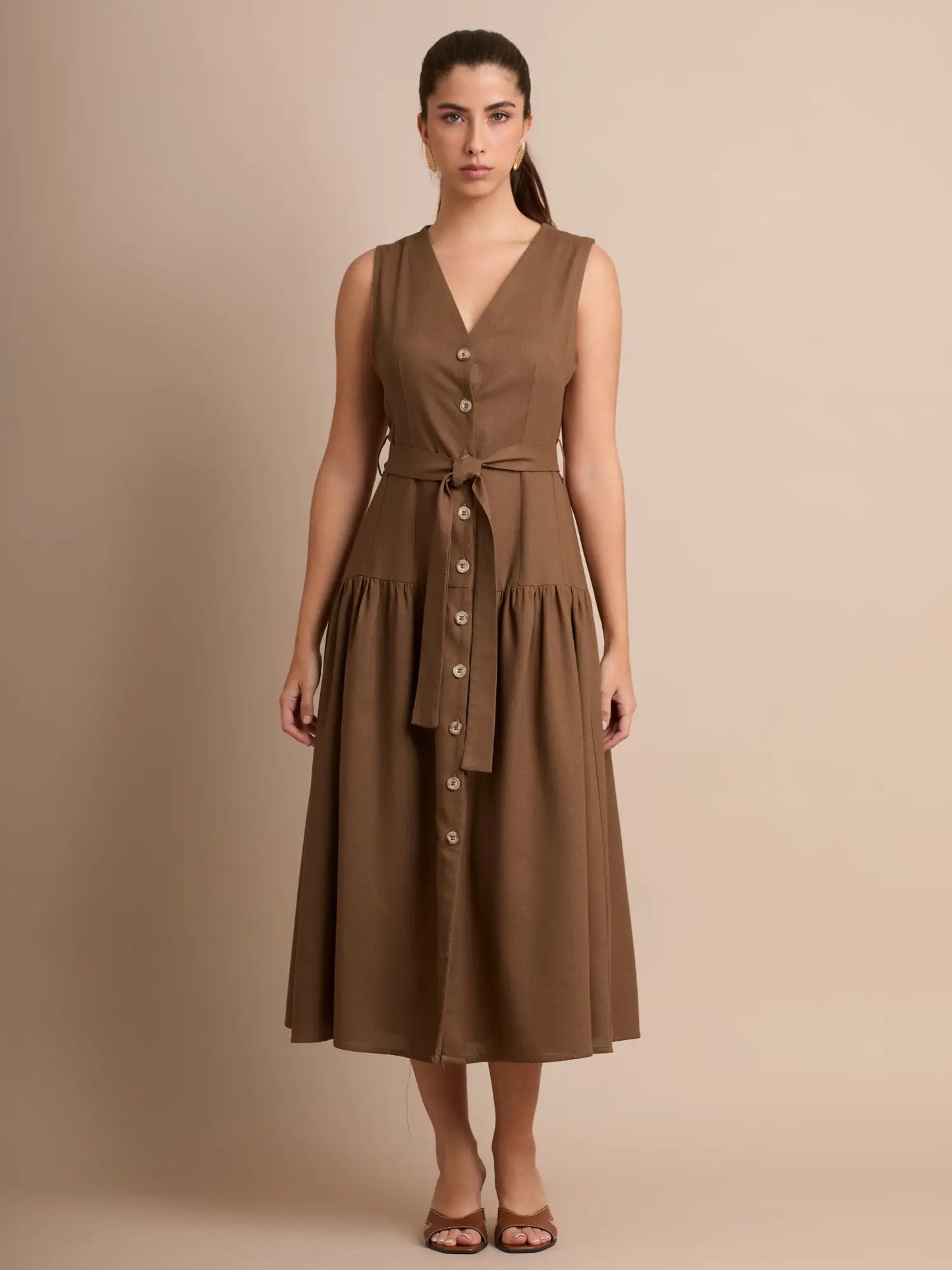 Un vestido sin mangas que combina clasicismo y modernidad, con escote en V y botones que recorren el frente. Su falda amplia añade movimiento y una sensación ligera.