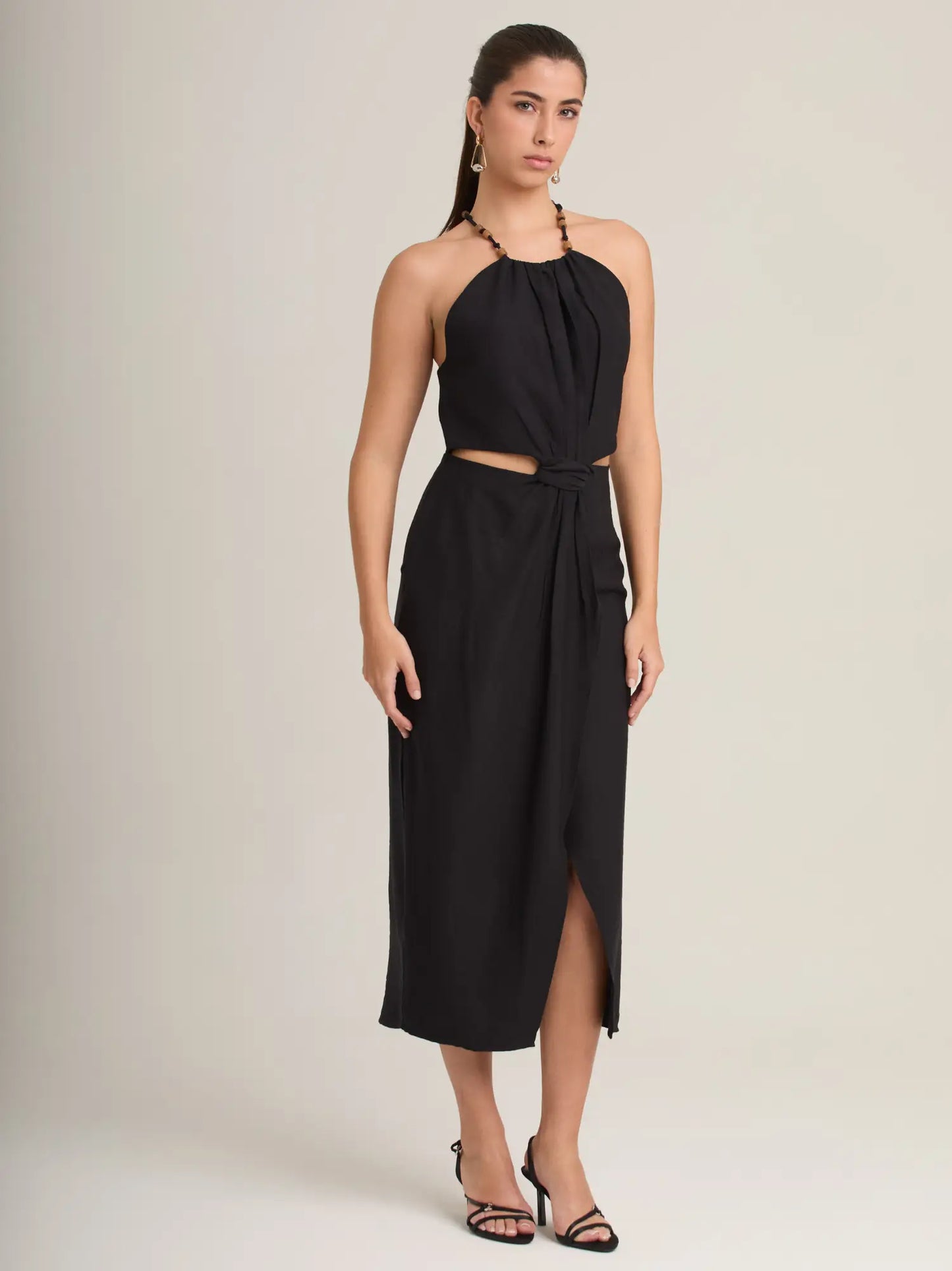 Este vestido midi negro ofrece un diseño sofisticado con cuello halter adornado y una abertura frontal que aporta movimiento. Ideal para cenas, fiestas o eventos formales donde busques un look impactante.