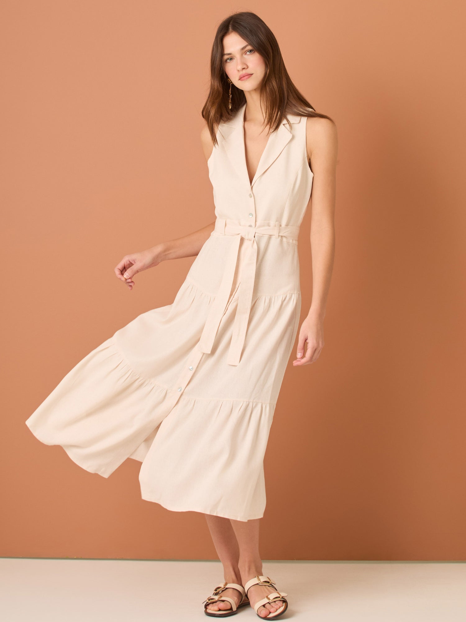 Vestido midi sin mangas con solapa tipo sastre, botonadura frontal y corte en la cintura que se ajusta con lazo, terminado en falda con volantes amplios