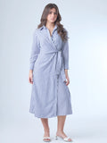 Vestido camisero midi con diseño de rayas verticales. Tiene cuello clásico, mangas largas con puños y un corte cruzado al frente que se ajusta con un lazo a la cintura. La falda cae con movimiento sutil y el ajuste en la cintura define la silueta de forma favorecedora. Es una prenda cómoda, estructurada y con un aire sofisticado.

Detalles:

Color: Azul
