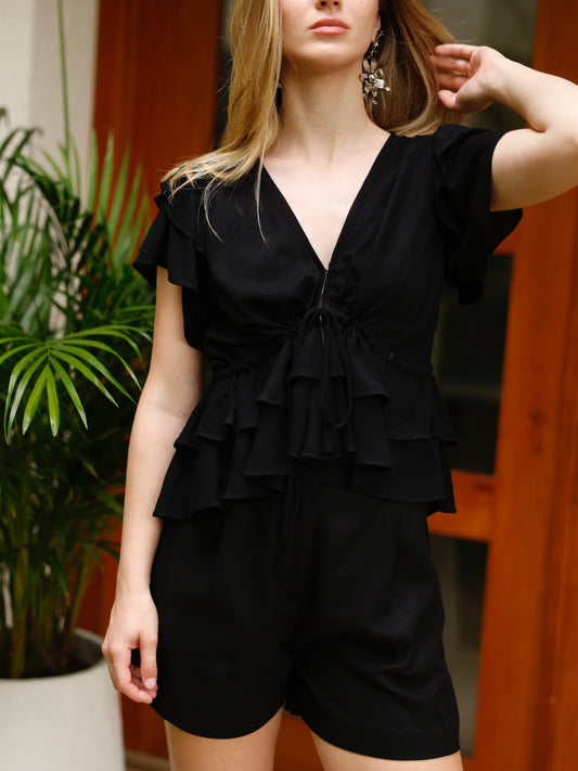 Blusa de escote en V profundo con detalle de amarre frontal. Presenta volantes en las mangas y doble capa de volantes en la parte inferior, lo que le aporta un toque femenino y romántico. El ajuste en la cintura crea una silueta favorecedora y delicada.

Detalles:

Color: Negro

Material: 100% poliéster

Cuidado: Lavar a mano con jabón suave, por separado.No dejar en remojo. Planchar a temperatura alta.