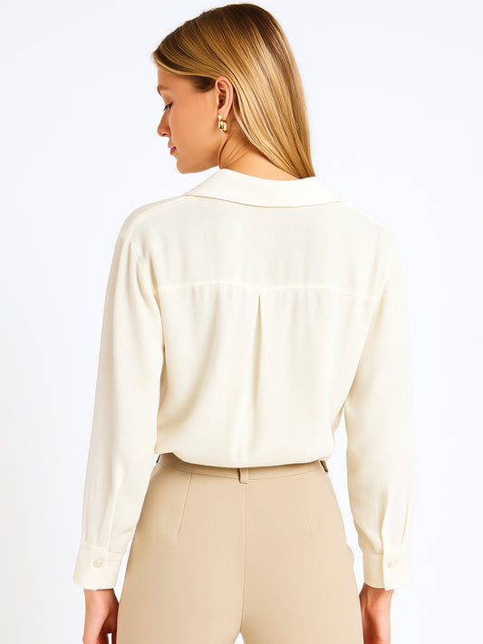 Esta blusa de manga larga tiene un estilo sofisticado y moderno. Presenta cuello clásico tipo camisero y un diseño de escote en "V" sutil que alarga visualmente el cuello. El detalle más destacado es el nudo frontal retorcido en la parte baja, que genera un efecto drapeado y asimétrico, aportando dinamismo y elegancia a la prenda. Los puños son anchos y estructurados, lo que refuerza el acabado pulido del diseño. Ideal para looks formales o smart-casual, combinada con pantalones de tiro alto o faldas.