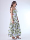 Este vestido largo presenta un diseño fresco y moderno con estampado botánico en tonos verde oliva, verde lima y azul claro sobre fondo blanco. Tiene tirantes anchos y escote recto, que aportan estructura y realzan los hombros. Los laterales descubiertos le dan un toque contemporáneo y femenino, acentuando la figura de forma sutil. La falda cae en línea recta con un corte bajo y un ligero fruncido, lo que aporta movimiento y una silueta relajada. Es una prenda ideal para climas cálidos y ocasiones casuales 