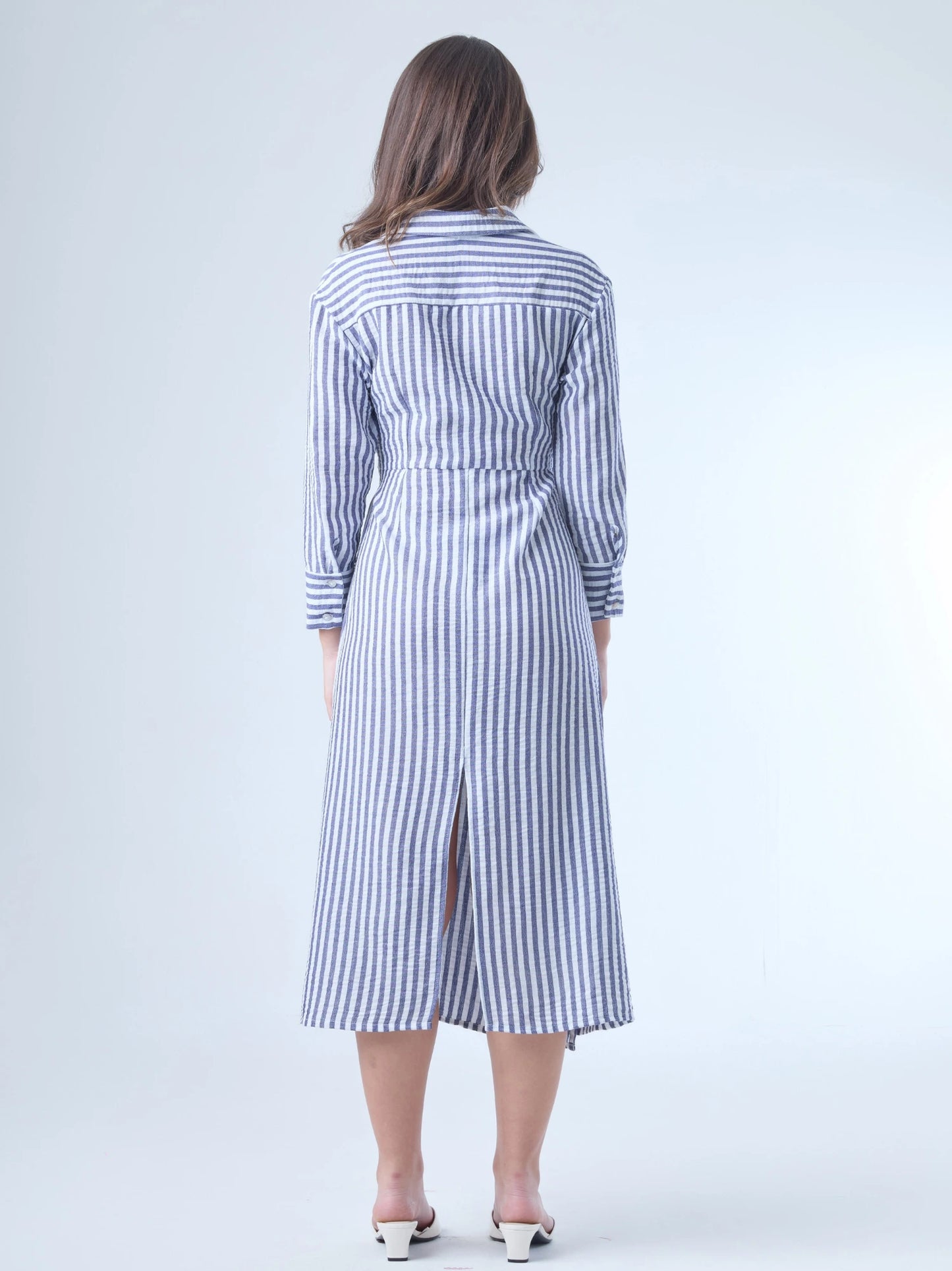 Vestido camisero midi con diseño de rayas verticales. Tiene cuello clásico, mangas largas con puños y un corte cruzado al frente que se ajusta con un lazo a la cintura. La falda cae con movimiento sutil y el ajuste en la cintura define la silueta de forma favorecedora. Es una prenda cómoda, estructurada y con un aire sofisticado.

Detalles:

Color: Azul